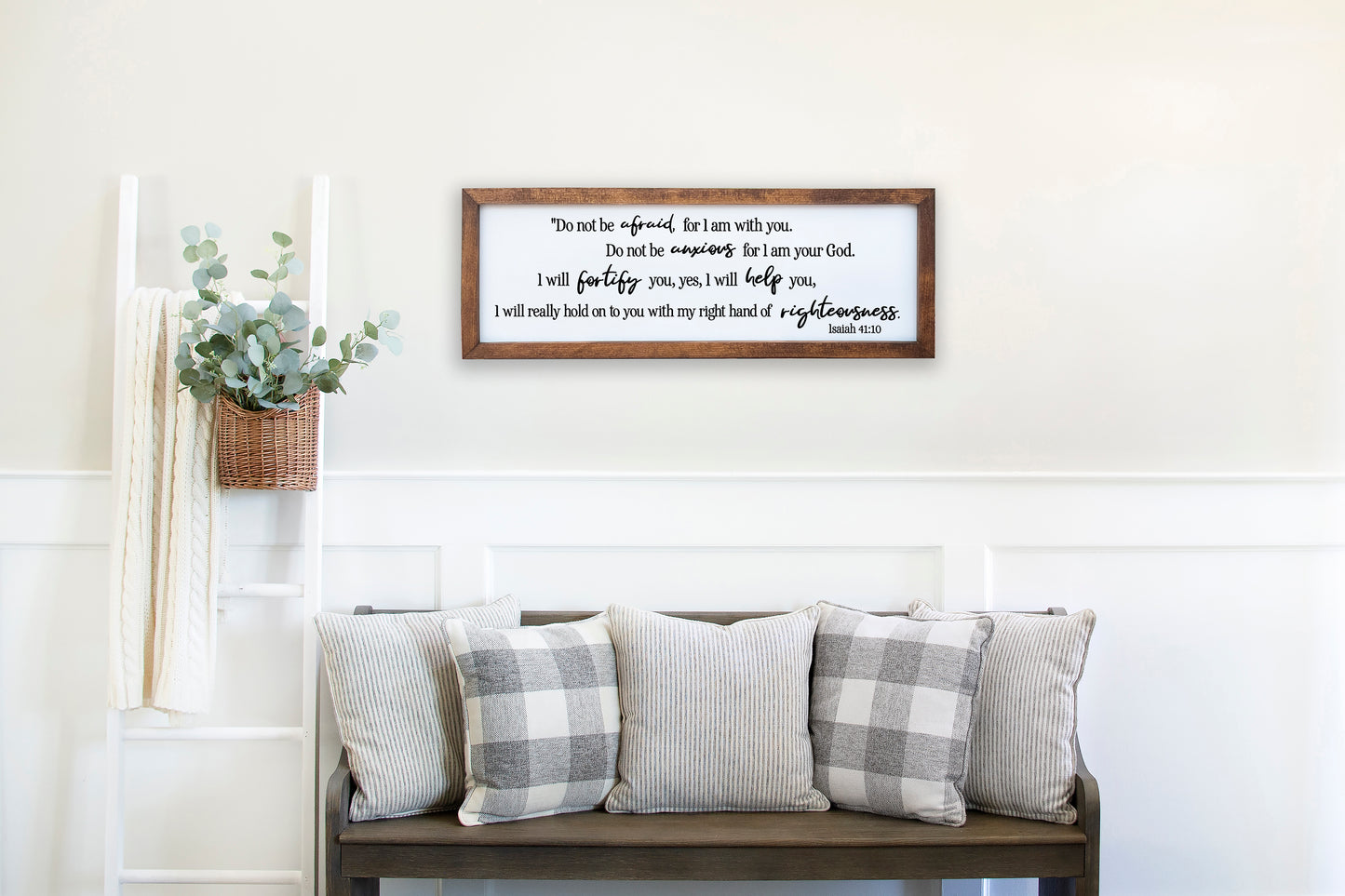Decorative pillows on a bench with a framed quote above in a home setting.