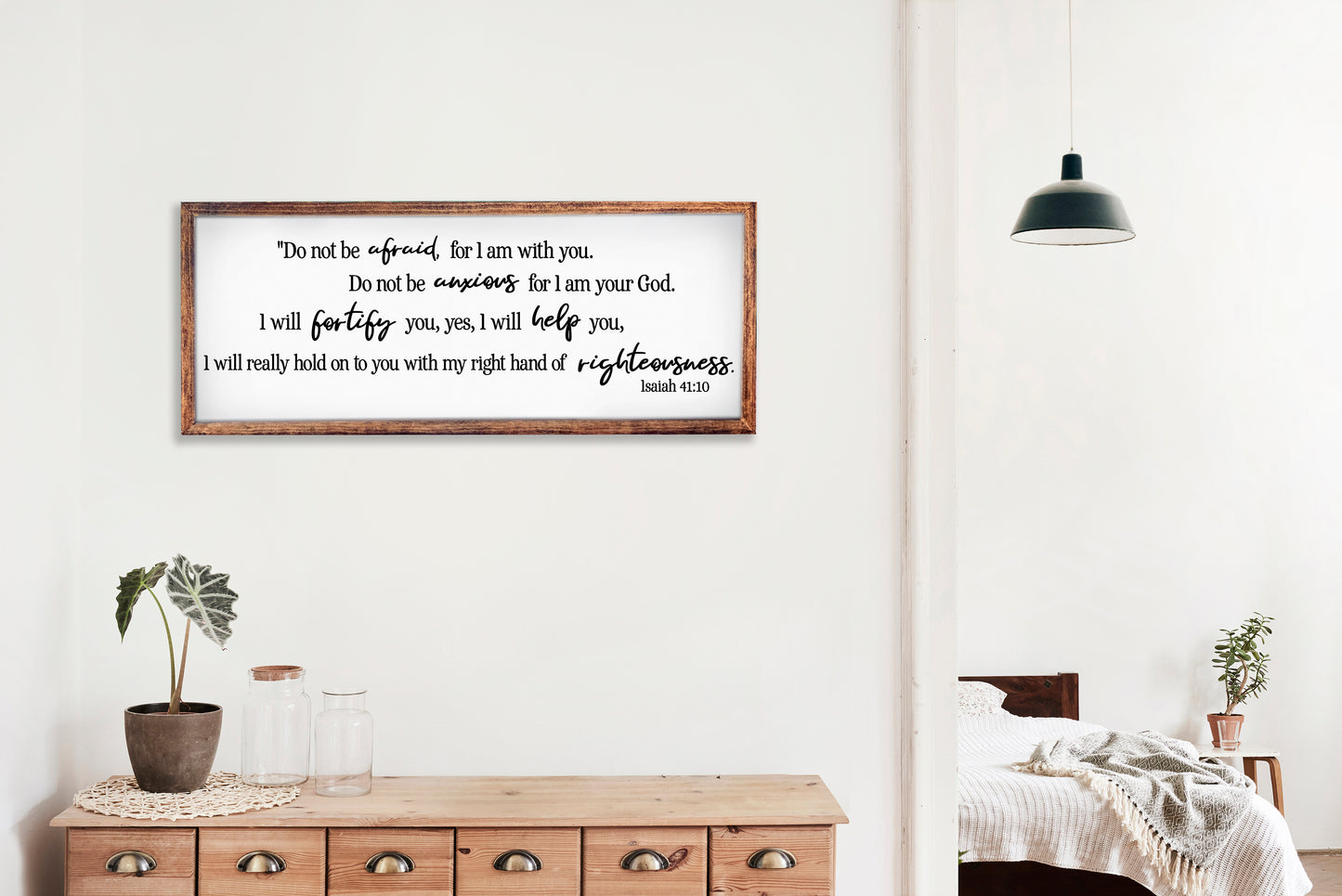 Framed motivational quote on a wall in a home setting with a wooden dresser and plants.