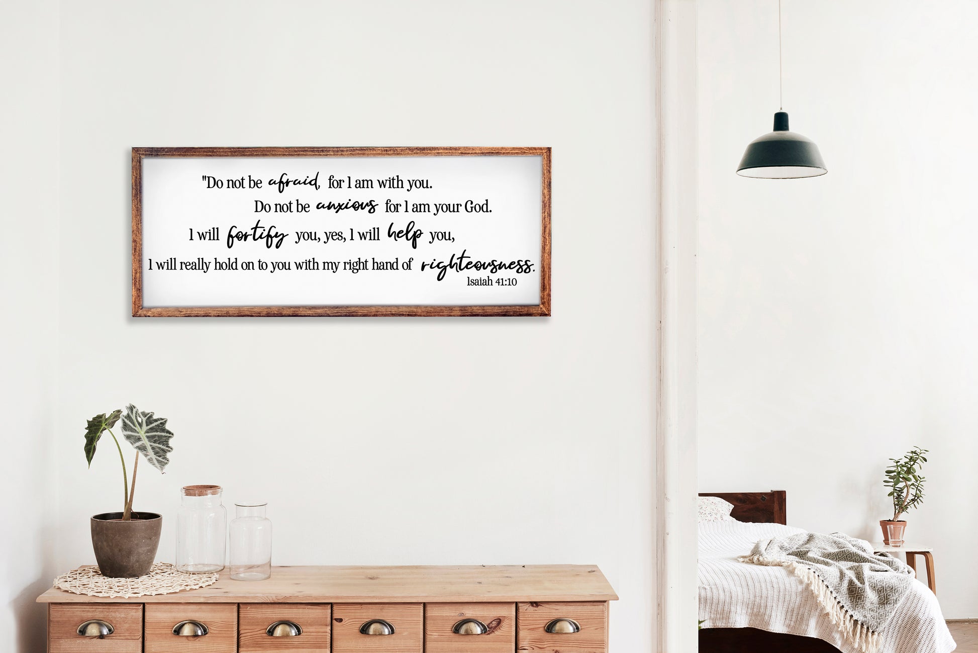 Framed motivational quote on a wall in a home setting with a wooden dresser and plants.