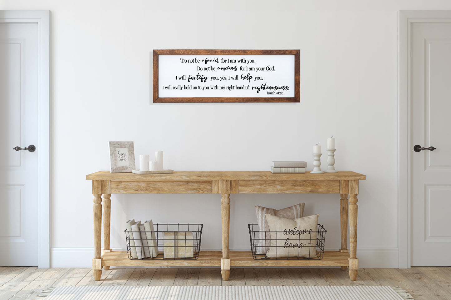 Wooden console table with decorative items against a white wall with a framed quote.