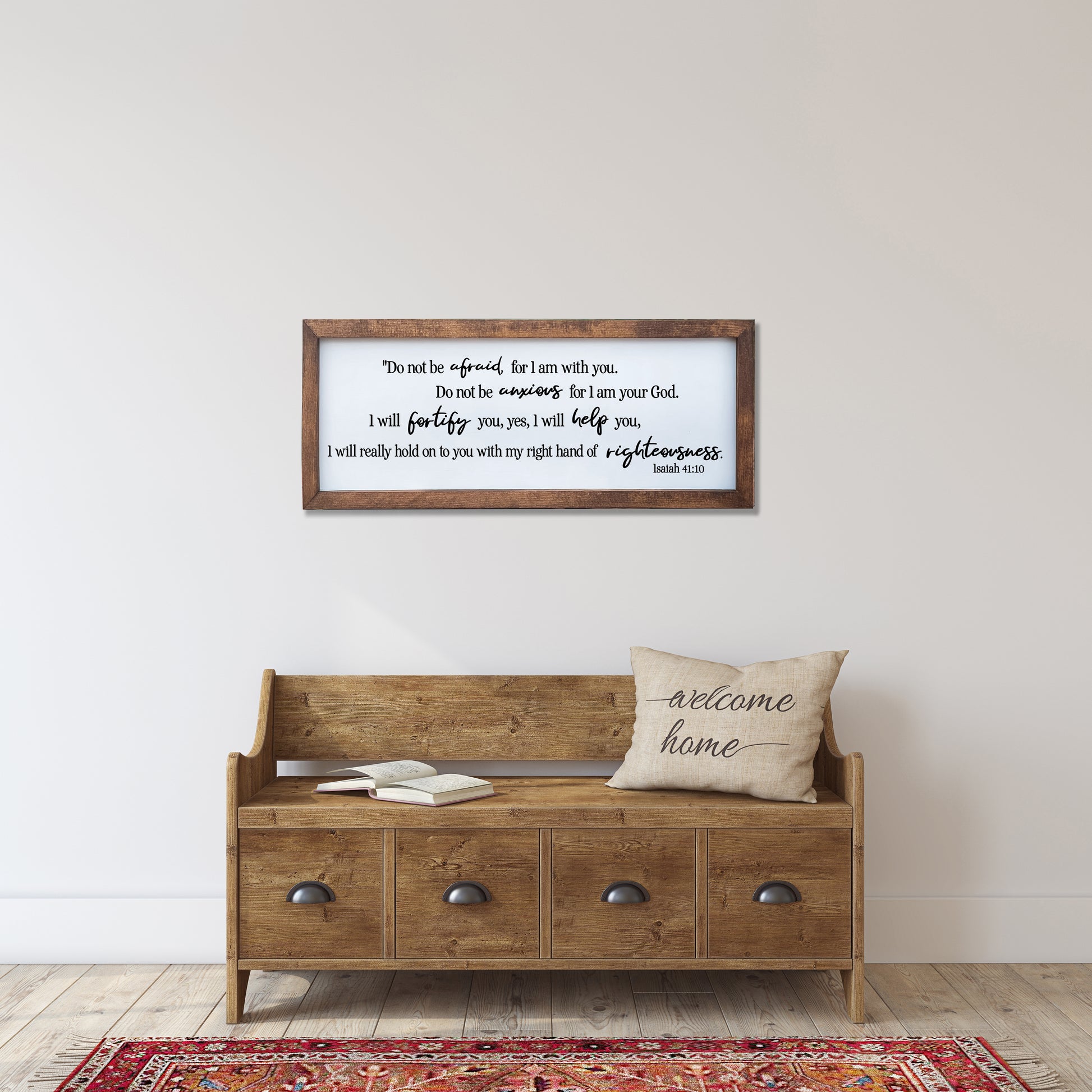 Wooden bench with drawers, cushion, and framed text on a wall in a room.