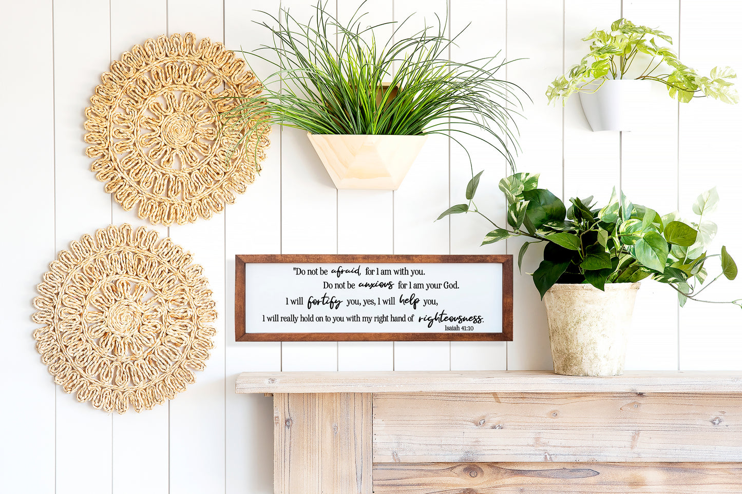 Decorative wall shelf with plants, woven coasters, and a framed quote on a wooden surface.