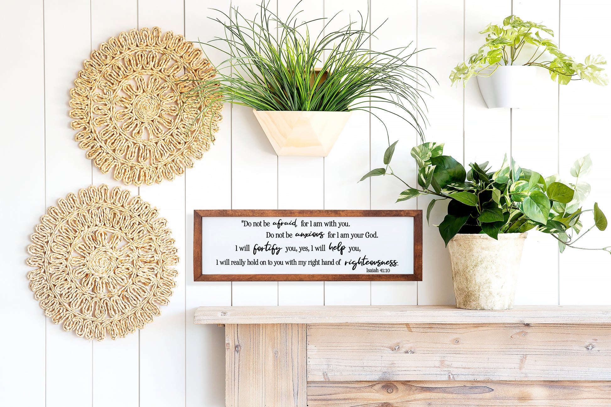 Decorative wall shelf with plants, woven coasters, and a framed quote on a wooden surface.